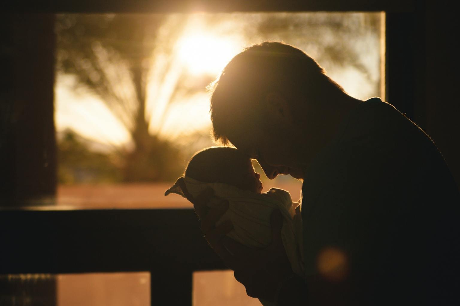 Silhouette of a father holding his newborn at sunset, highlighting love and connection.