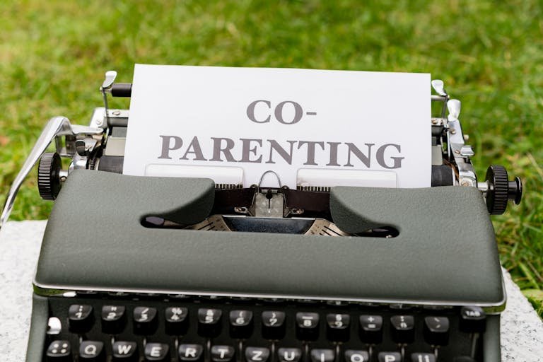 Close-up of an antique typewriter with 'Co-Parenting' paper, set outdoors on grass.