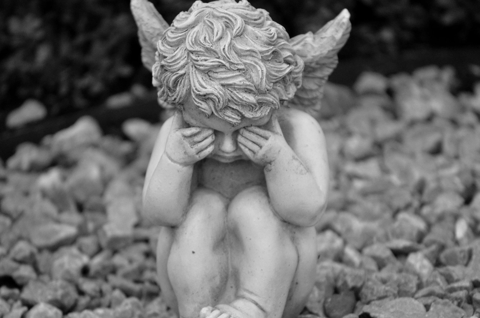 Black and white image of an angel statue covering its eyes, evoking sadness and contemplation.